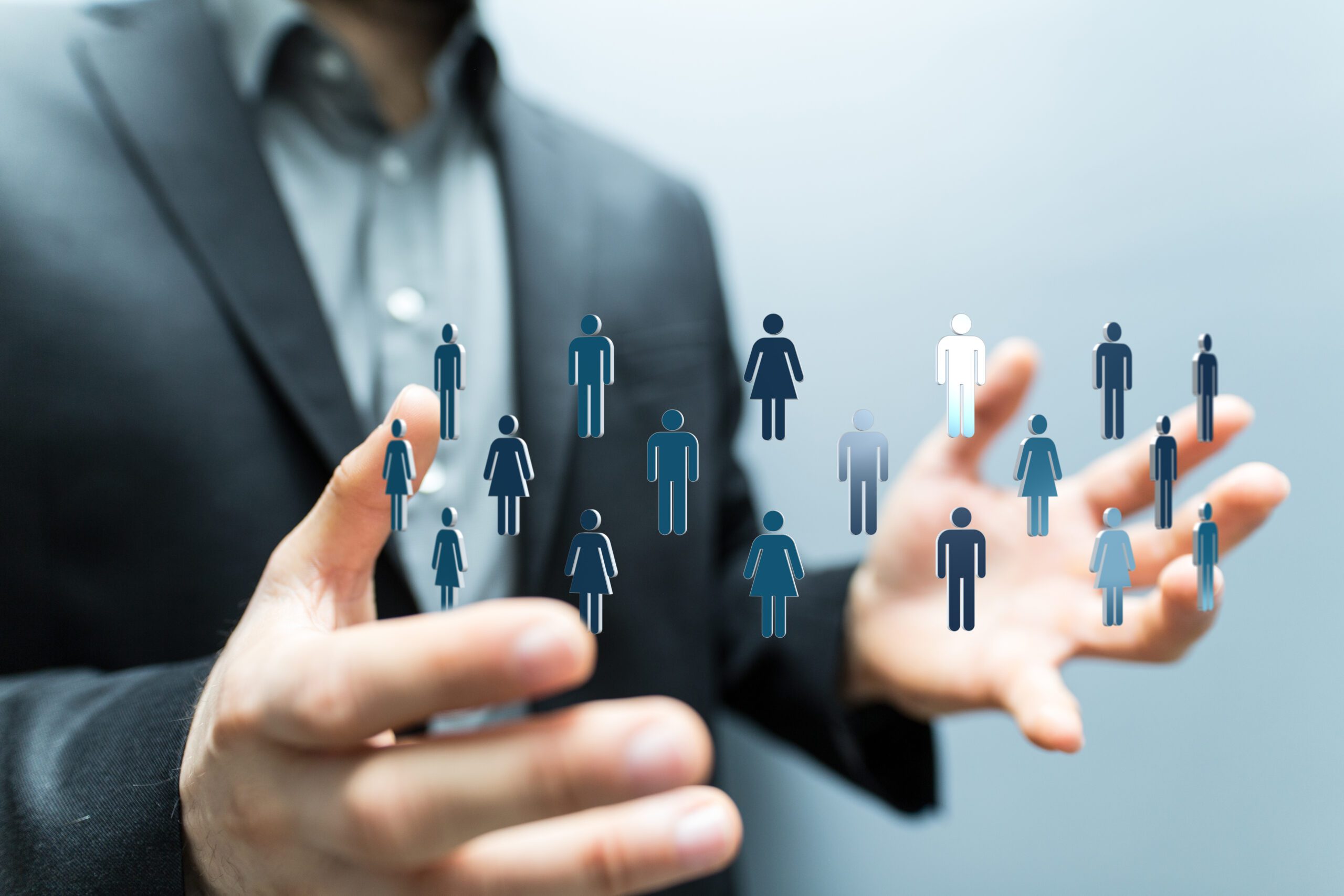 A person in a suit holds their hands open with digital icons of men and women floating between them, symbolizing human resource management or networking.